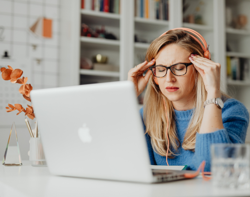 Jeune femme blonde dans son bureau en face de son ordinateur qui est très fatiguée et qui porte un casque audio orange
