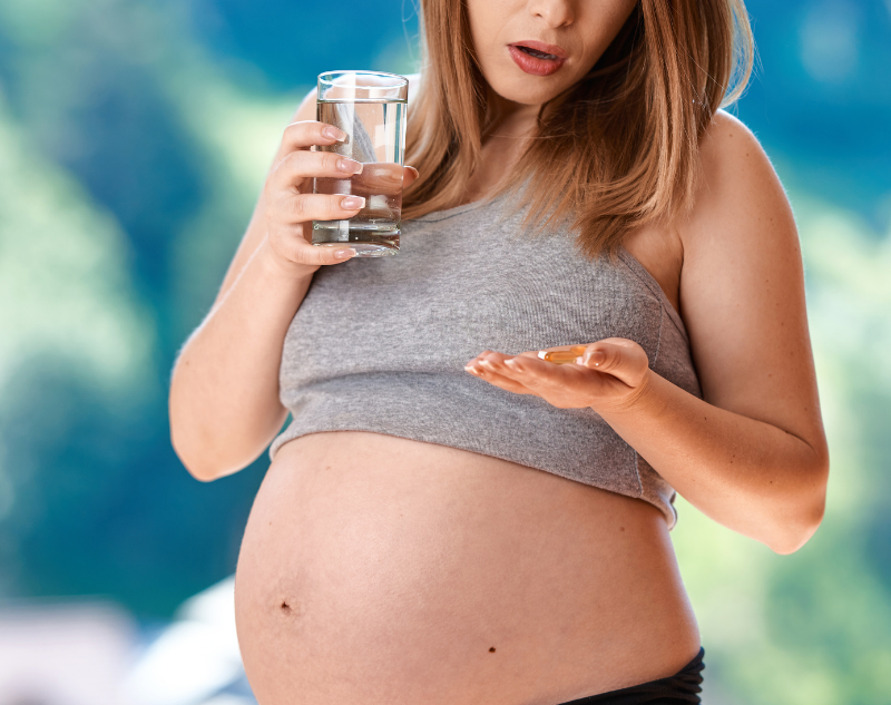 Femme enceinte avec le ventre à l'air qui tient un verre d'eau et ses compléments alimentaires