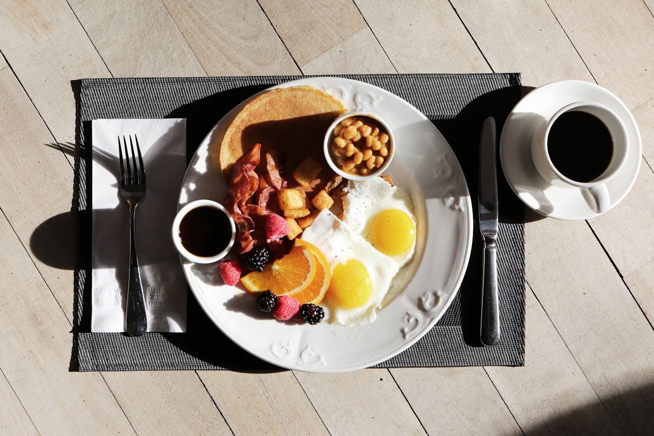 Petit-déjeuner salé avec des oeufs, du bacon, des pancakes, des fruits et du café.