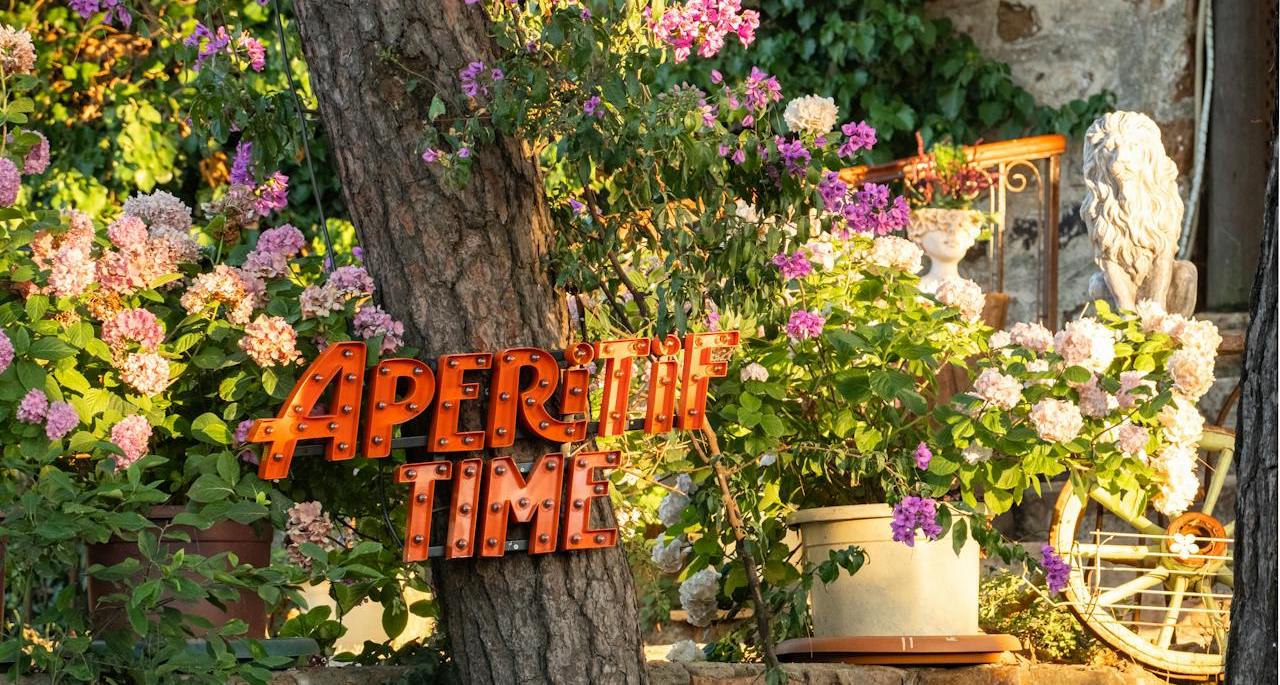 Photo d'un arbre et de fleurs avec un écriteau lumineux marqué "apéritif time"
